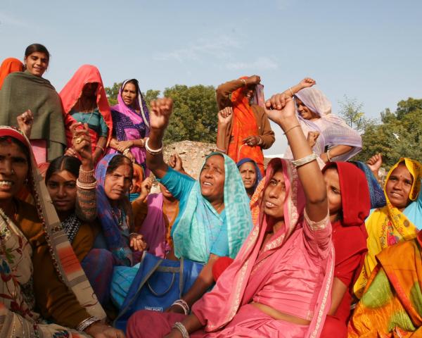 A group of women in colorful clothing raise their fists in unity.